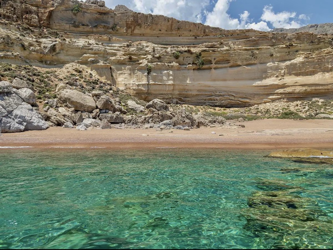 Secluded Rhodes beach with clear turquoise water framed by layered cliffs