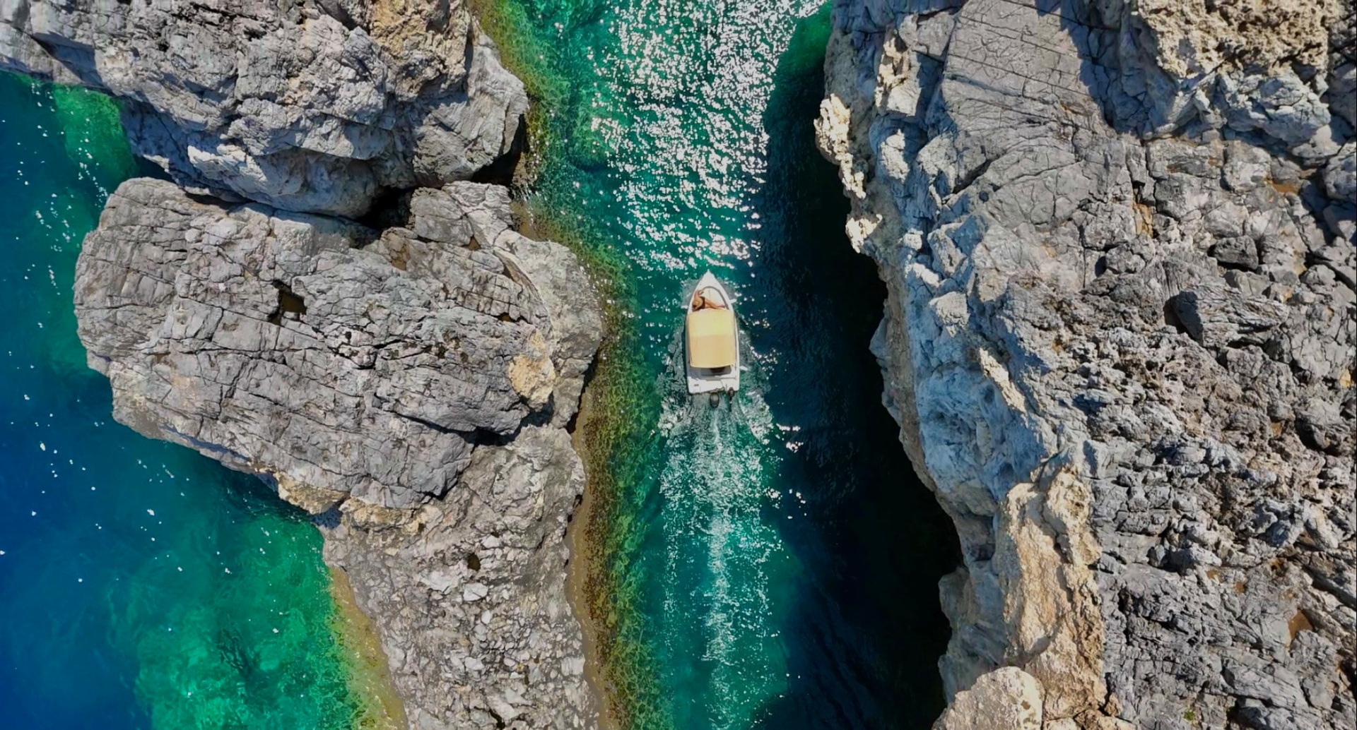 Aerial view of a RÉMA boat cruising between rocky cliffs in turquoise water