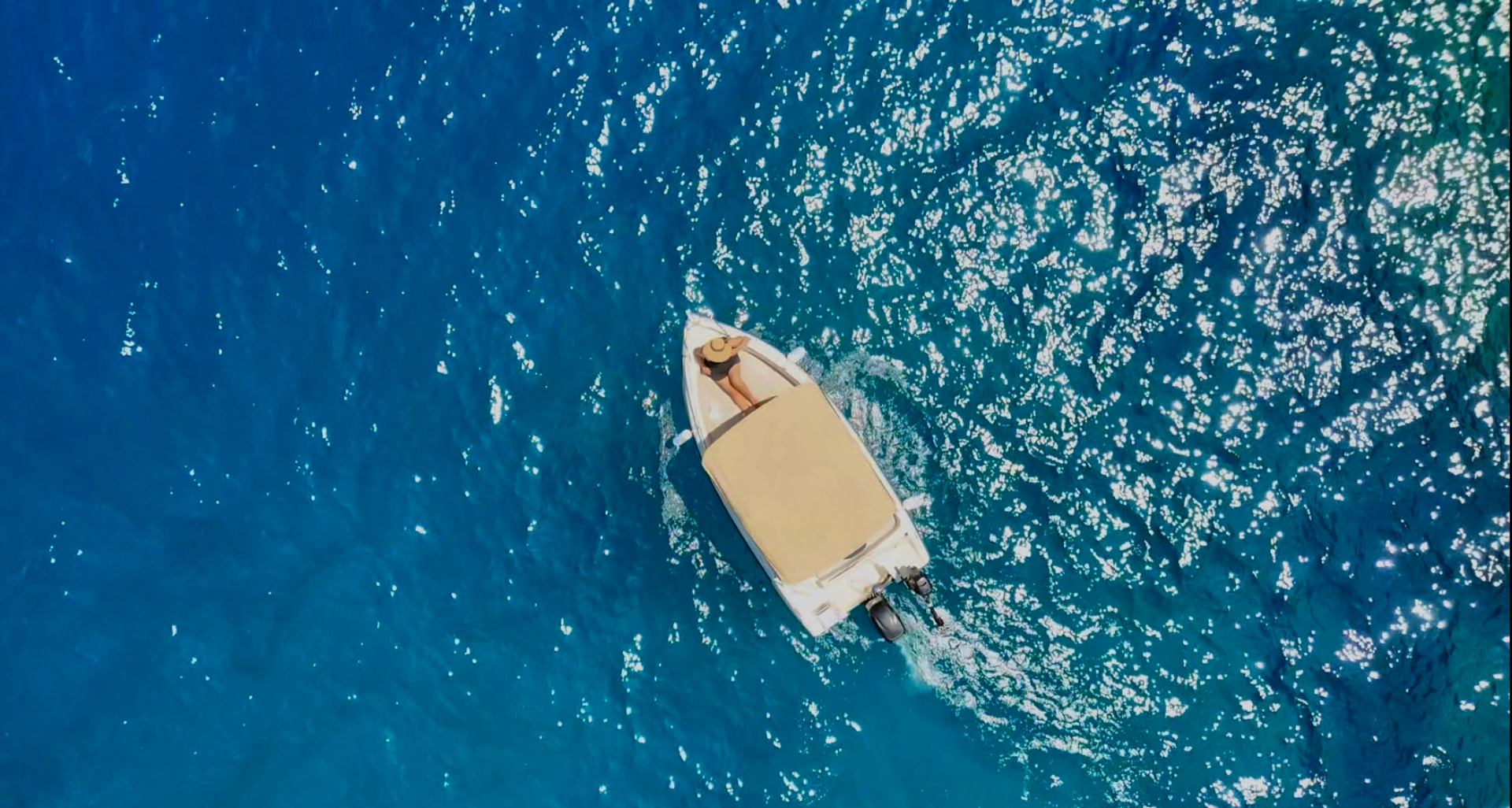 Guest sunbathing on the bow of a RÉMA boat on a glittering blue sea